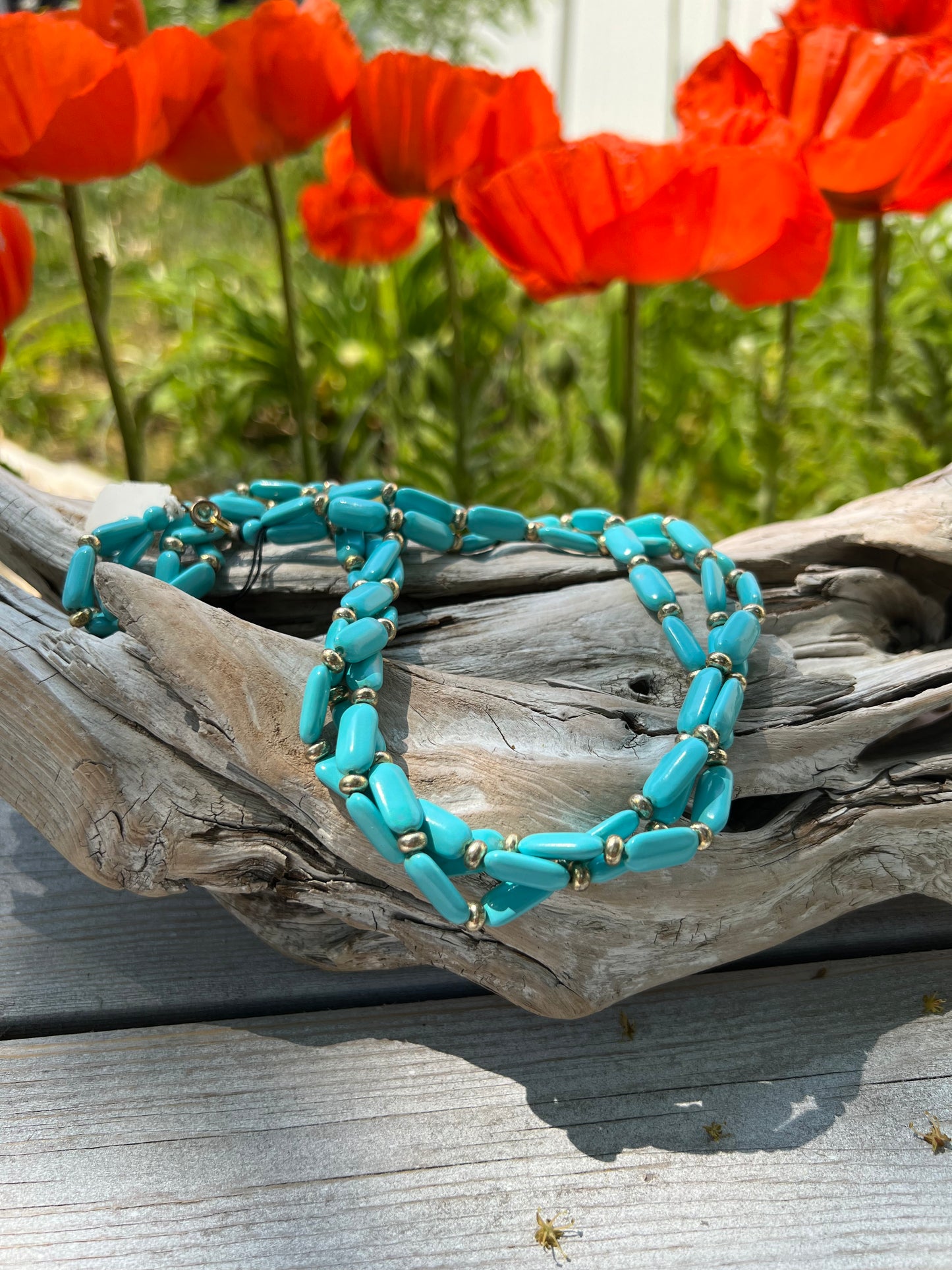 A vintage twisted turquoise beaded necklace displayed on a wooden surface with poppies in the background.