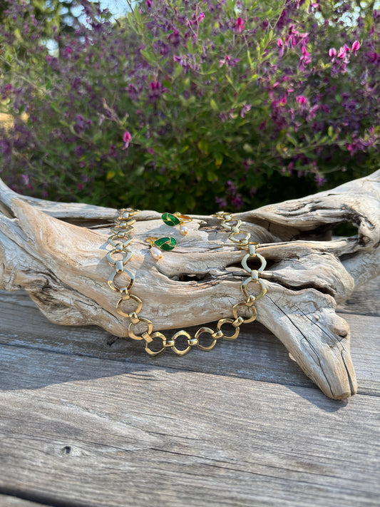 Gold bracelet with green gemstones on a wooden surface with purple flowers in the background