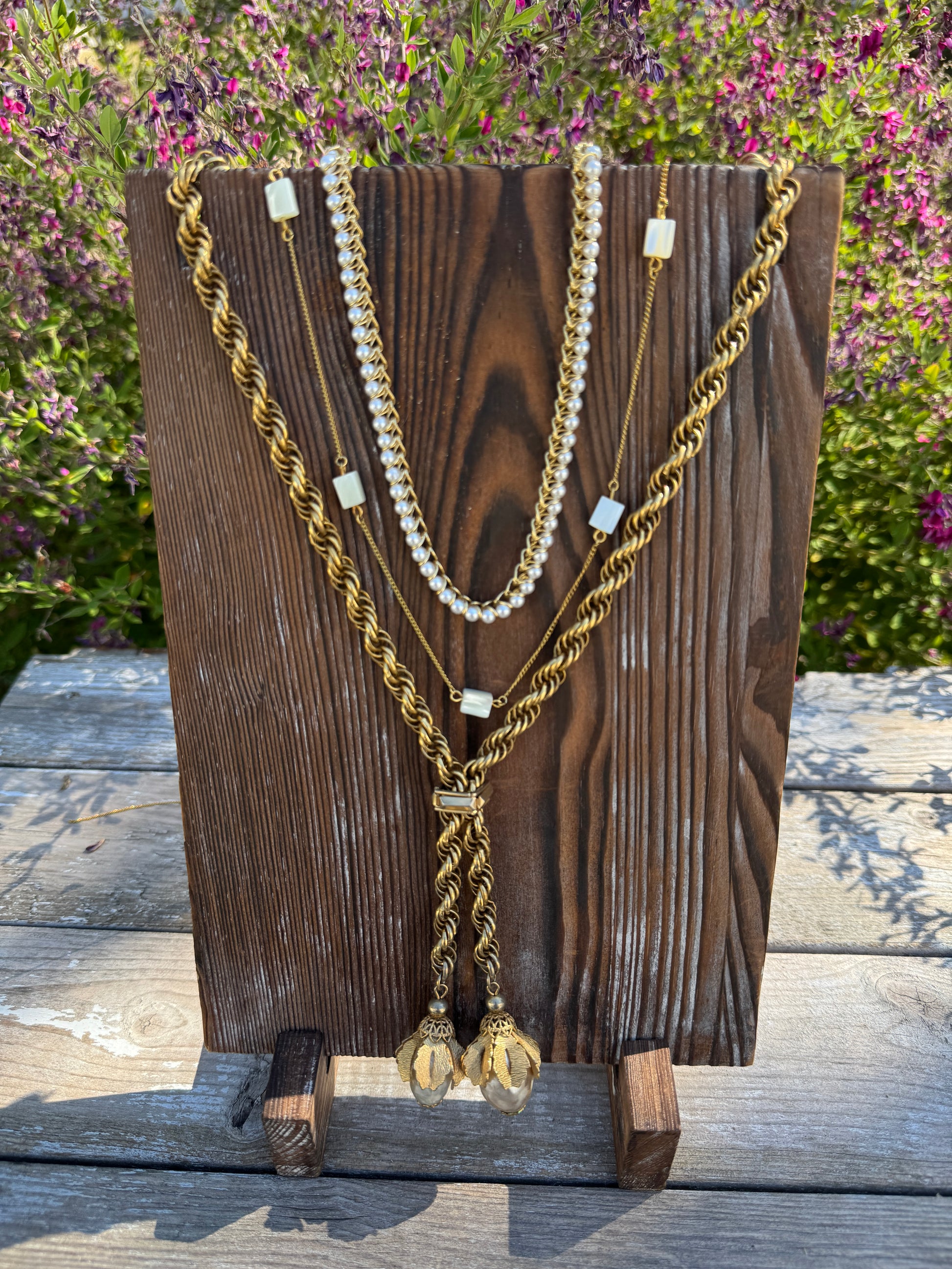 Set of gold and pearl necklaces on a wooden board with a natural outdoor background