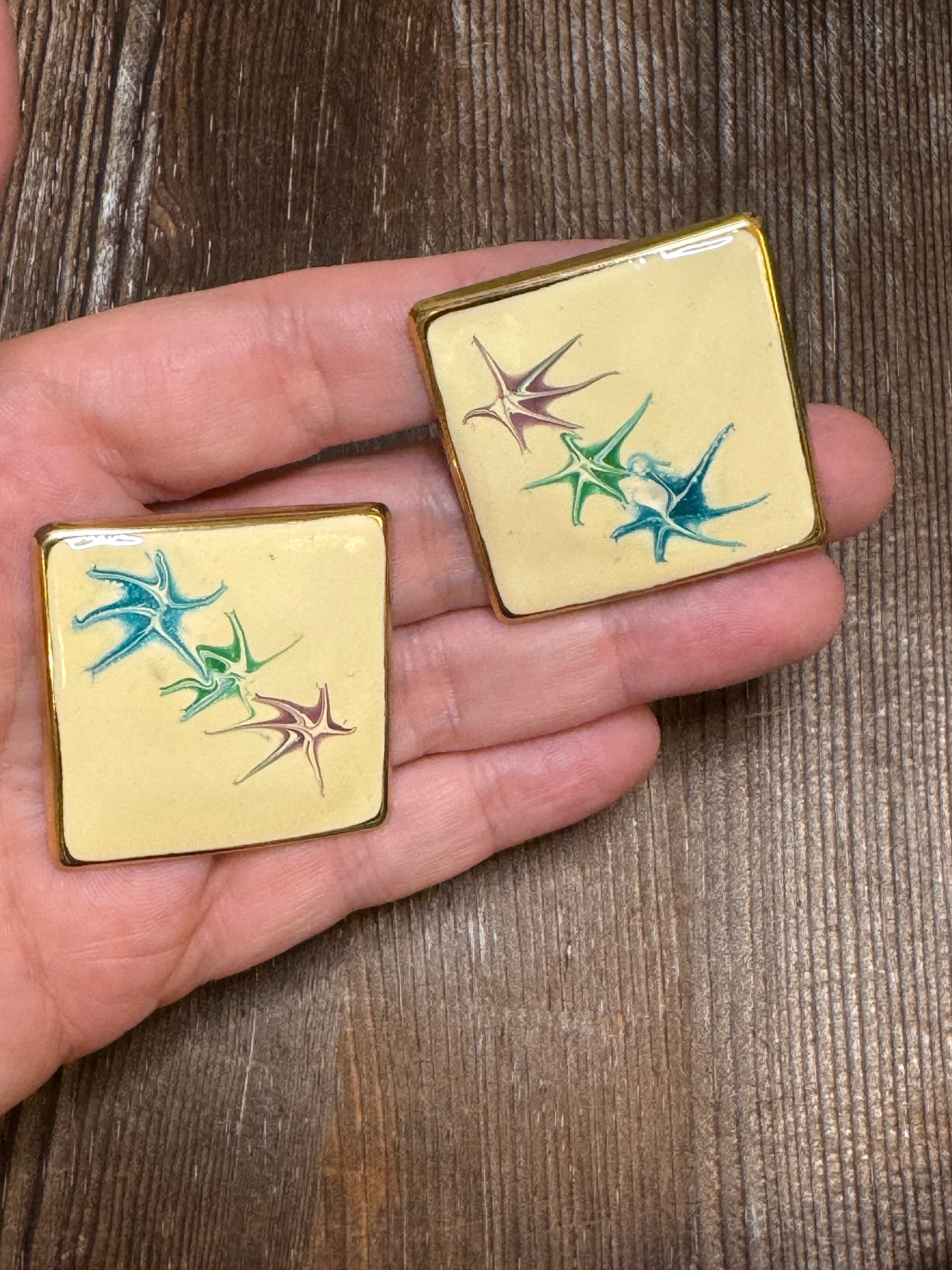 Two small gold boxes with colorful designs held in a hand on a wooden surface