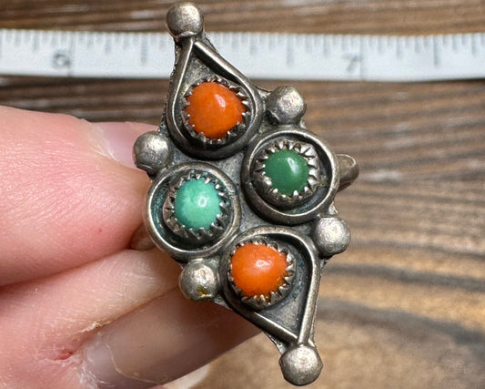 Silver ring with colored stones held by a hand against a wooden background