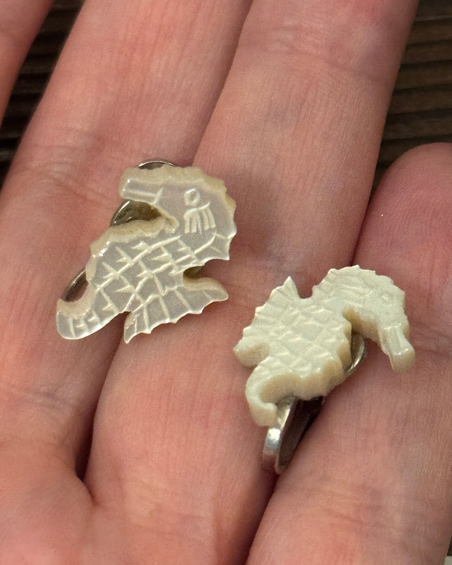 Two seahorse-shaped earrings held in a hand.