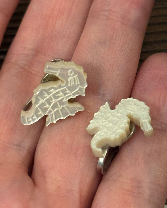 Two seahorse-shaped earrings held in a hand.